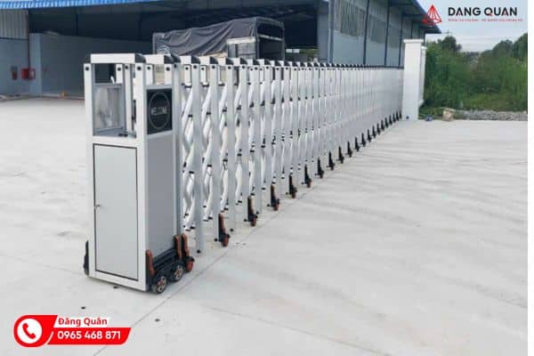 Cổng xếp hợp kim nhôm DQ22 màu trắng bạc duỗi dài trên sân bê tông, đầu kéo hộp đỉnh phẳng có ô đèn và biển WELCOME