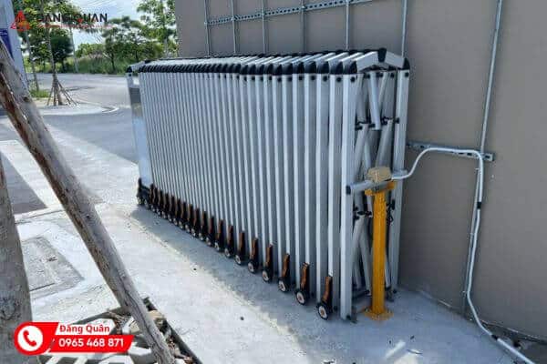 Thân cổng xếp nhôm DQ24 màu trắng bạc dồn gọn sát tường bên đường, nắp chụp sẫm màu trên đỉnh nan