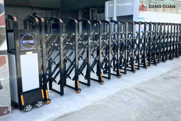Cổng xếp tự động thân nhôm màu đen, khung đỉnh bo tròn, đầu kéo có màn hình chữ WELCOME, lắp trước nhà xưởng