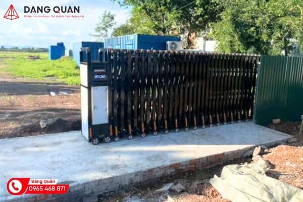 Cổng xếp nhôm màu đen xếp gọn về phía đầu kéo, lắp trên nền bê tông mới trong khuôn viên nhà xưởng