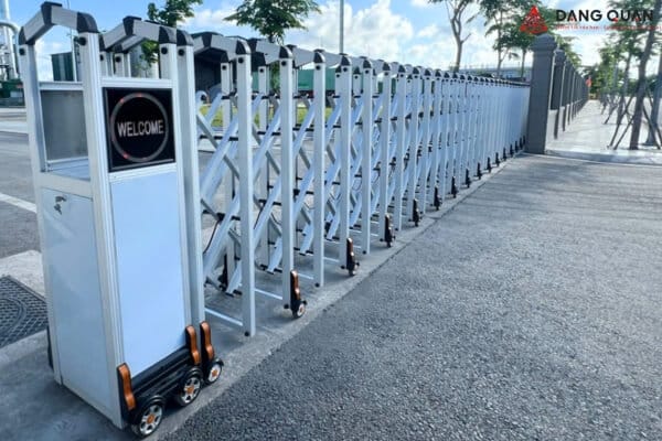 Cổng xếp tự động màu bạc, khung đỉnh phẳng, đầu kéo có màn hình hiện chữ WELCOME, lắp dọc vỉa hè