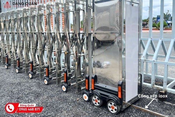 Đầu kéo cổng xếp inox tự động đặt trên cụm bốn bánh xe, thân nan inox bóng phía sau
