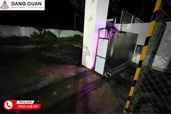 Cổng xếp tự động khép sát trụ cổng lúc trời tối, bên cạnh hàng rào lưới và cột sơn vạch vàng đen
