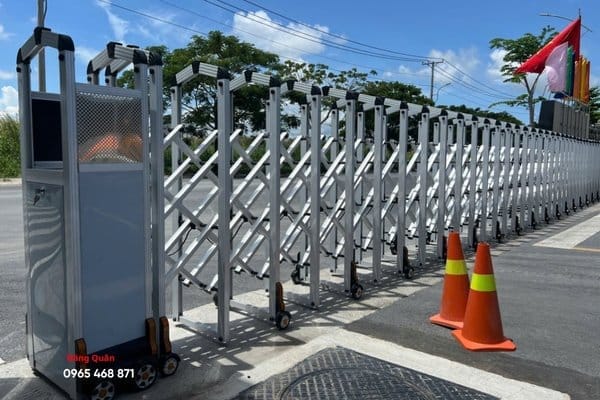 Cổng xếp tự động màu bạc ở lối vào rộng, hai cọc tiêu giao thông đặt trước đầu kéo