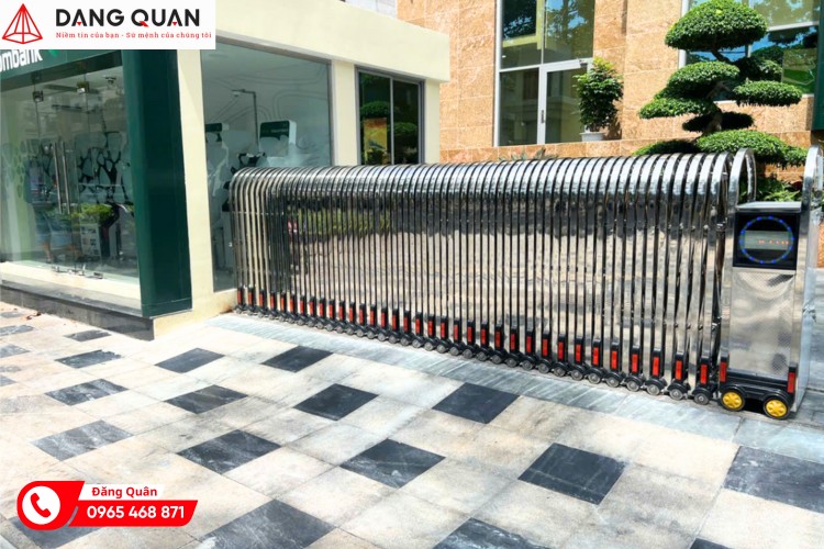 Cổng xếp inox tự động đóng trước mặt tiền cửa hàng có cây cảnh và nền lát gạch